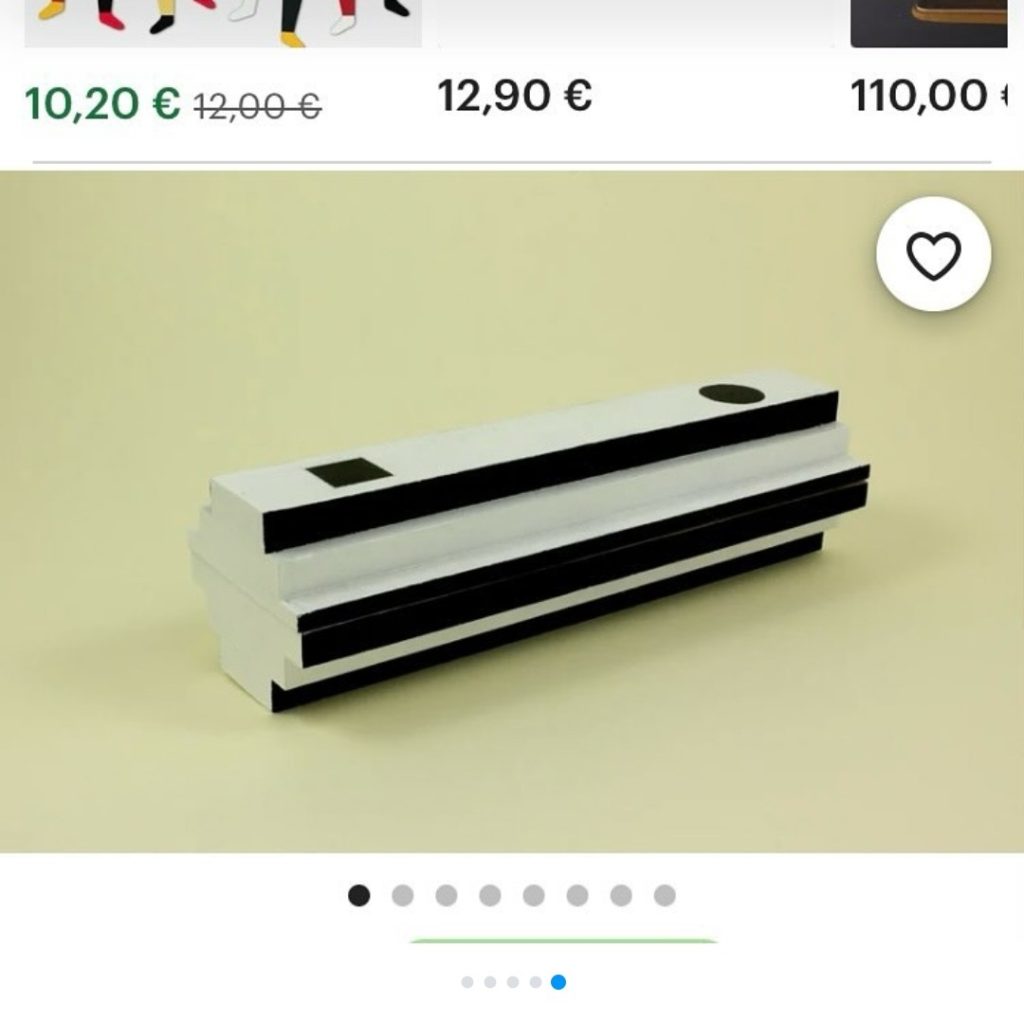 screencap d'une photo d'une maquette en bois d'un cercueil. L'objet ressemble à une sculpture suprématiste, peint en noir et blanc.